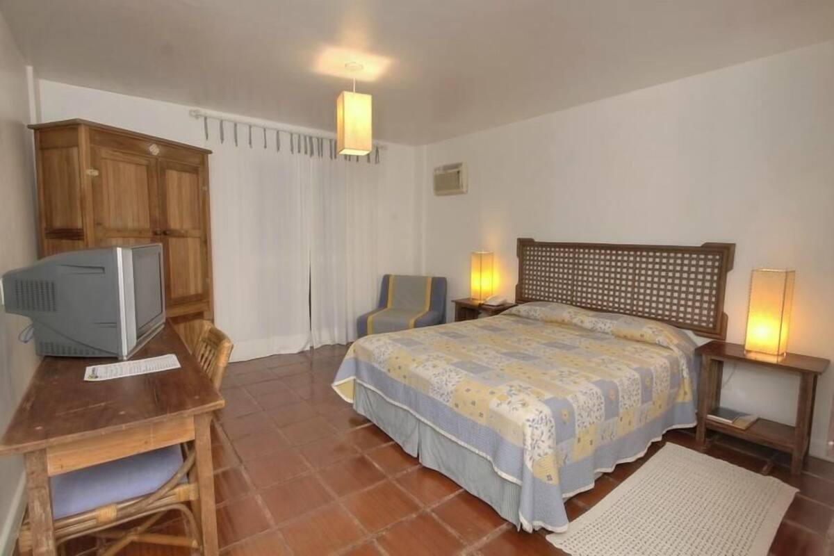 Ein Schlafzimmer mit einem Bett, einem Schreibtisch mit Computer, einem Stuhl und zwei Nachttischlampen.