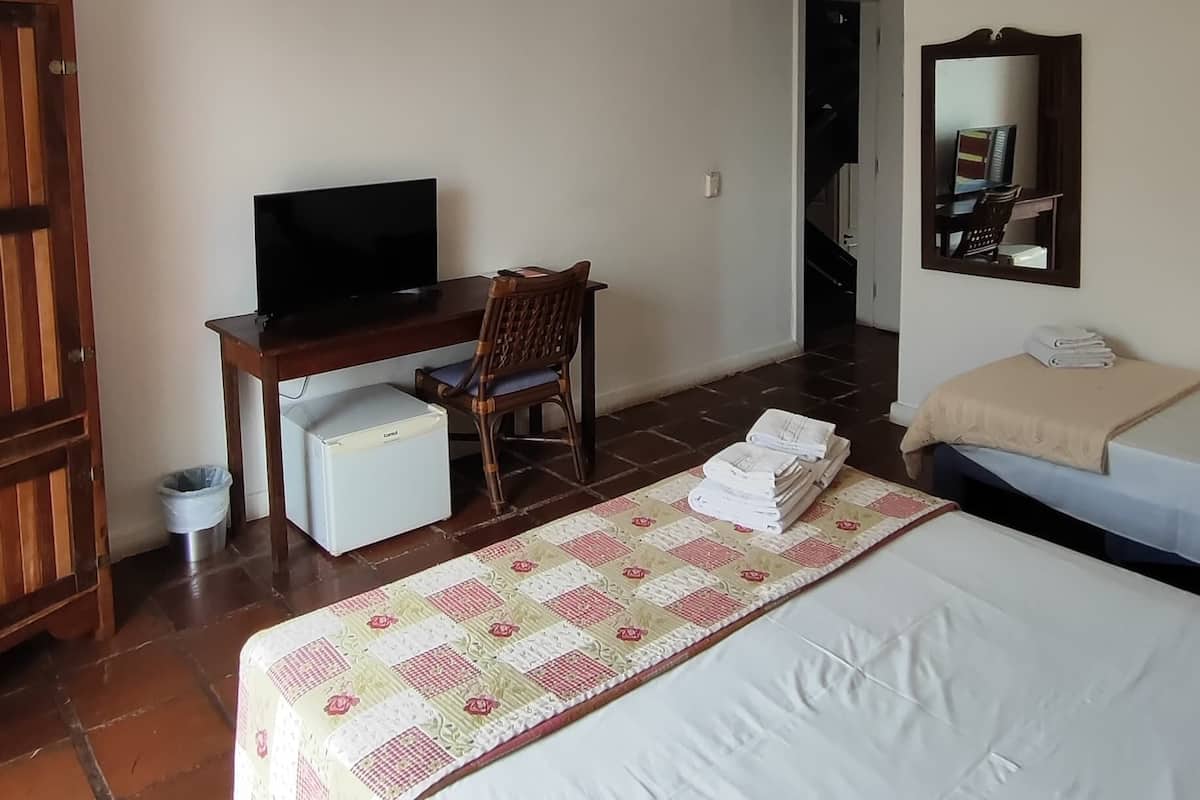 Ein Hotelzimmer mit Bett, Schreibtisch mit Fernseher, Stuhl, Kleiderschrank und Badezimmer mit Spiegel.