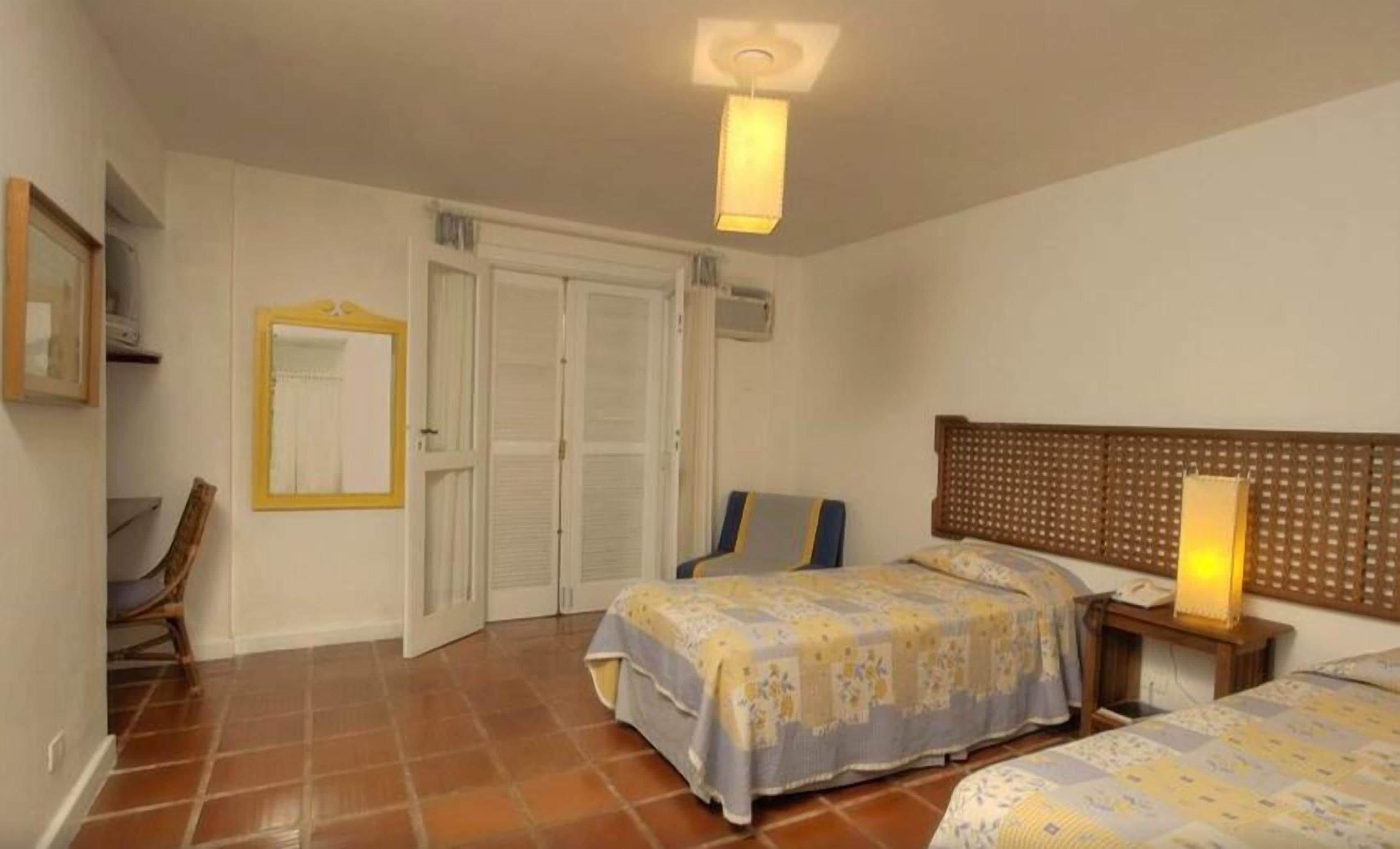 A bedroom with two beds, a mirror, a chair, and a bedside table with a lamp.