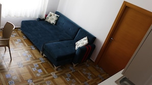 A room with a blue sofa, patterned cushions, a wooden floor with tiles, a chair, and a door. - Mercan Suite Hotel (Gökçeada)