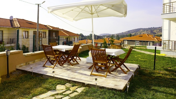 An outdoor patio area with a table and chairs, a large umbrella, and a view of surrounding buildings. - Mercan Suite Hotel (Gökçeada)