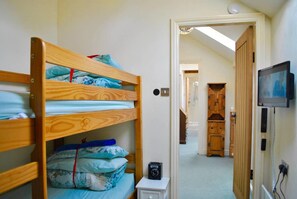 A bedroom with bunk beds, a small bedside table, a television, and a wooden cabinet.