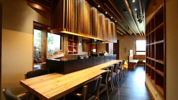 A restaurant with a long wooden counter, cushioned chairs, and a high ceiling with wooden beams.