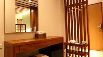 A hotel room with a wooden desk, a mirror, a small bench, and a wooden partition.