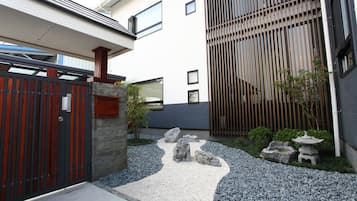A modern building with a gated entrance, a stone pathway, and a small garden area with rocks and a stone lantern.