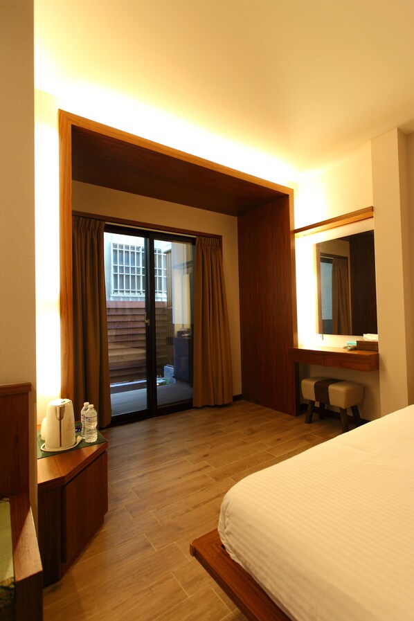 Habitación de hotel con cama, escritorio, silla, espejo, cafetera y puerta corrediza de vidrio que da a un área exterior.