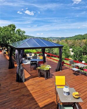 A wooden deck with outdoor furniture, a covered seating area, and a view of the surrounding landscape. - La Bayardine (Sarlat-la-Canéda)