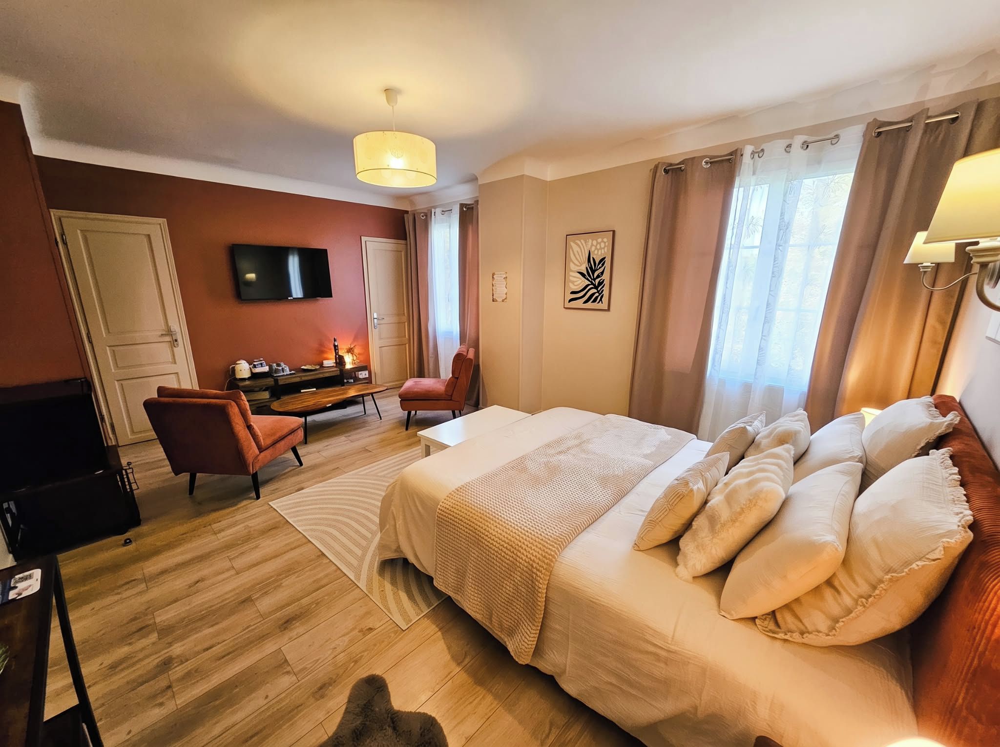 A hotel room with a large bed, a desk with a chair, a TV on the wall, and a window with curtains.