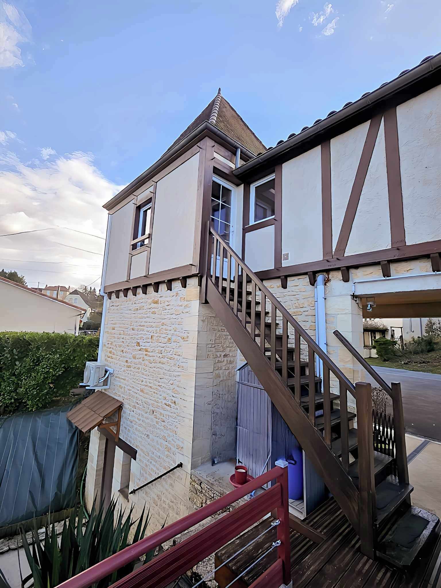 Une maison à deux étages avec une façade en pierre, un escalier en bois et un petit balcon.