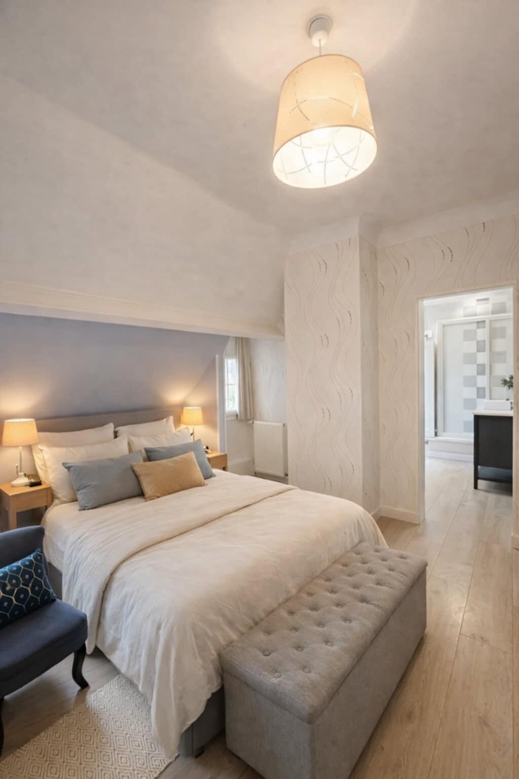 Une chambre à coucher avec un grand lit, des lampes de chevet, un banc et un luminaire au plafond.