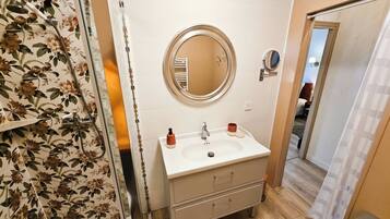 Un baño con lavamanos blanco, espejo redondo y ducha con papel tapiz floral.