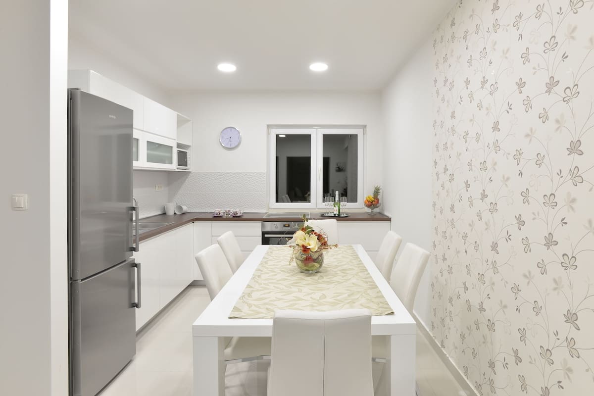 A modern kitchen with white cabinetry, a stainless steel refrigerator, a microwave, and a dining table with chairs.