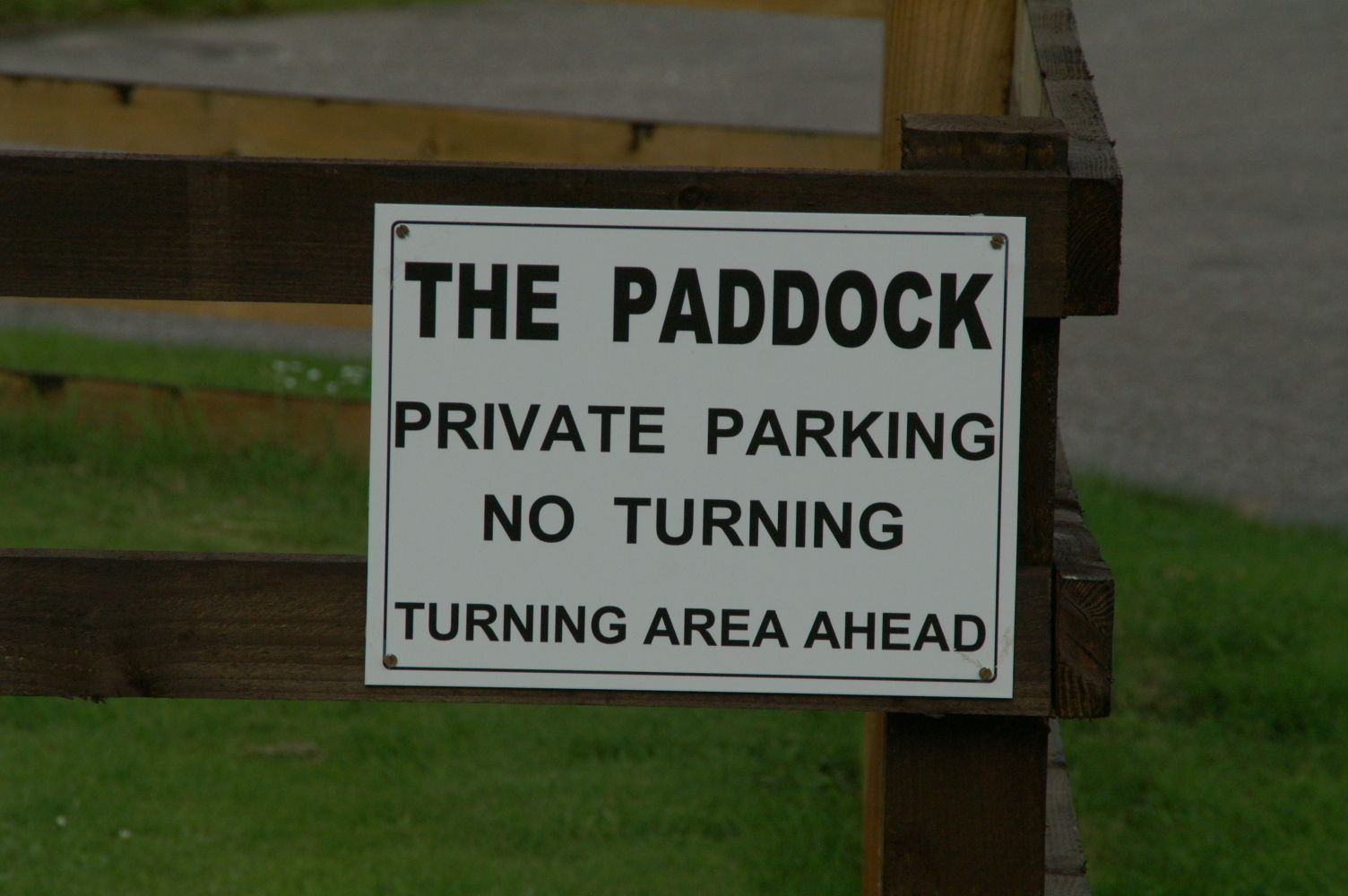 Schild an einem Holzpfosten mit der Aufschrift: 'THE PADDOCK PRIVATE PARKING' 'Keine Durchfahrt' 'Kreisförmige Fahrbahn folgt'.