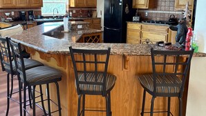 A modern kitchen with wooden cabinets, a black refrigerator, and a central island with bar stools. - Beautiful Mountain Home Near Yosemite (Groveland)