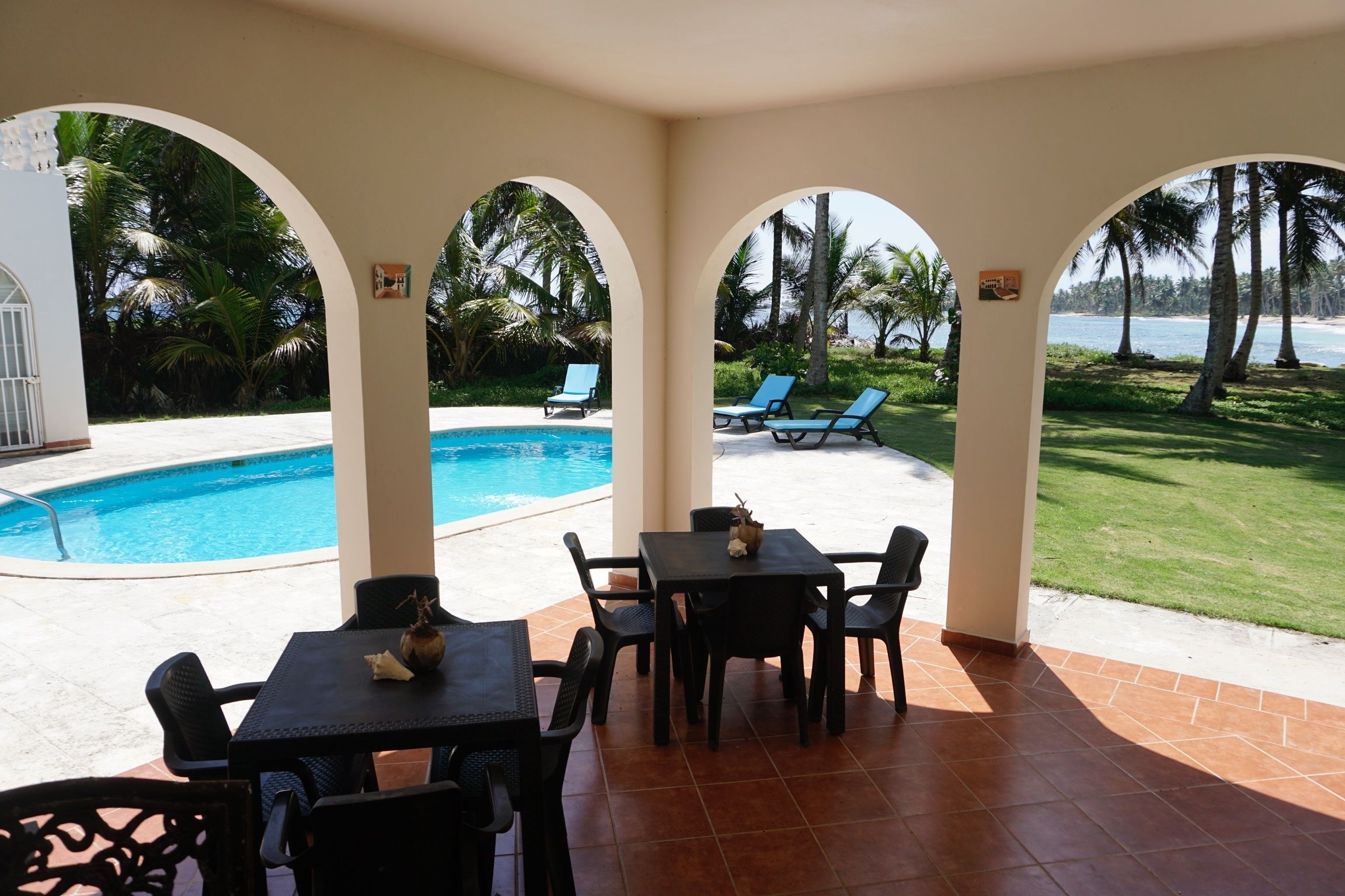 A covered outdoor area with a pool, lounge chairs, and a table with chairs.