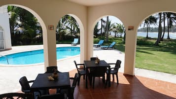 A covered outdoor area with a pool, lounge chairs, and a table with chairs.