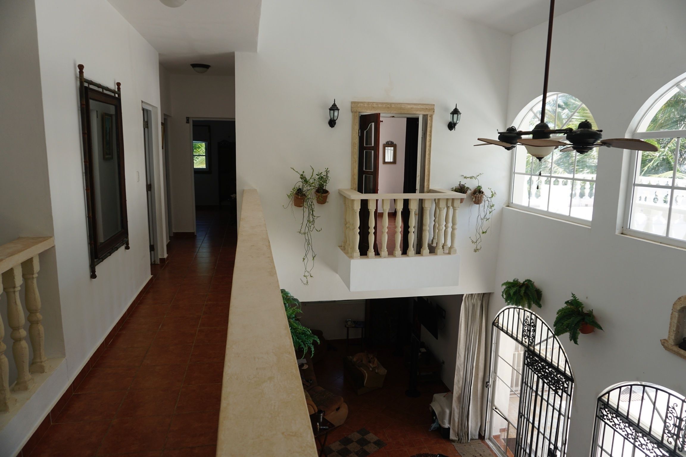 A spacious hallway with a high ceiling, a balcony with a railing, and multiple potted plants.