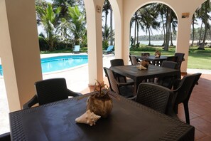 A poolside area with tables and chairs, a decorative shell, and a view of the pool and palm trees. - Baoba Breeze Bed & Breakfast (Cabrera)
