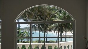 A room with a large arched window offering a view of a beach and palm trees. - Baoba Breeze Bed & Breakfast (Cabrera)