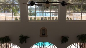 A room with large arched windows overlooking a pool area, a ceiling fan, and decorative plants. - Baoba Breeze Bed & Breakfast (Cabrera)
