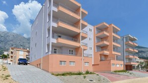 A multi-story residential building with balconies, a paved driveway, and a mountain backdrop. - Apartman Dominik (Makarska)