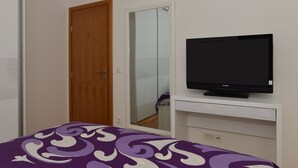 A bedroom with a bed, a TV on a stand, a wooden door, and a mirror. - Apartman Dominik (Makarska)