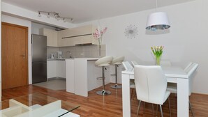 A modern kitchen with white cabinets, a stainless steel refrigerator, and a dining area with white chairs and a glass table. - Apartman Dominik (Makarska)