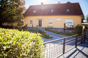 A yellow building with a red roof, a small garden, and a metal fence. - Treppendorfer Apartments (Burgebrach)