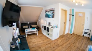 Ein modernes Wohnzimmer mit Flachbildfernseher, einer Couch, einem Couchtisch und einem Bücherregal.