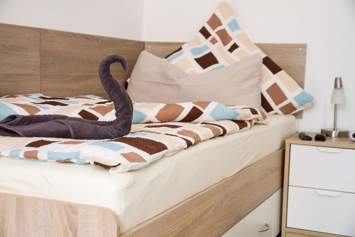 A neatly made bed with a patterned blanket, a wooden headboard, and a bedside table with a lamp.