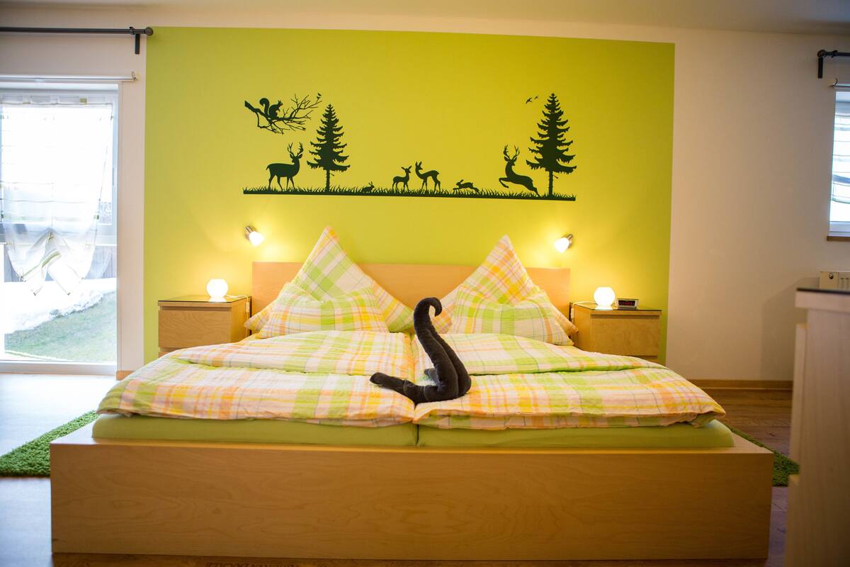 A bedroom with a bed, green walls, and a wall mural of animals and trees.