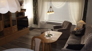 A cozy living room with a wooden coffee table, a sofa, a TV, and a lamp. - Ferienwohnung Braunlager Hexe (Braunlage)