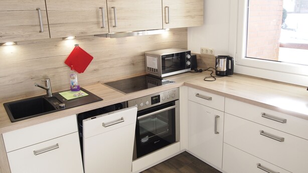 A modern kitchen with white cabinets, a stainless steel microwave, a dishwasher, and an oven. - Ferienwohnung Braunlager Hexe (Braunlage)