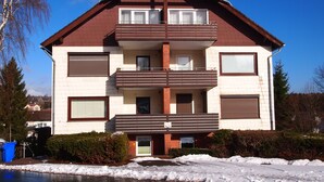 A multi-story residential building with a brown roof, white walls, and a balcony on the second floor. - Ferienwohnung Braunlager Hexe (Braunlage)