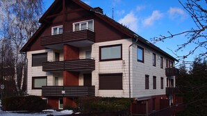 A multi-story residential building with a symmetrical facade, featuring a central entrance, balconies on each floor, and a visible chimney. - Ferienwohnung Braunlager Hexe (Braunlage)