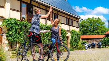 Dos personas en bicicleta frente a un edificio con tejado de azulejos y pared de piedra.