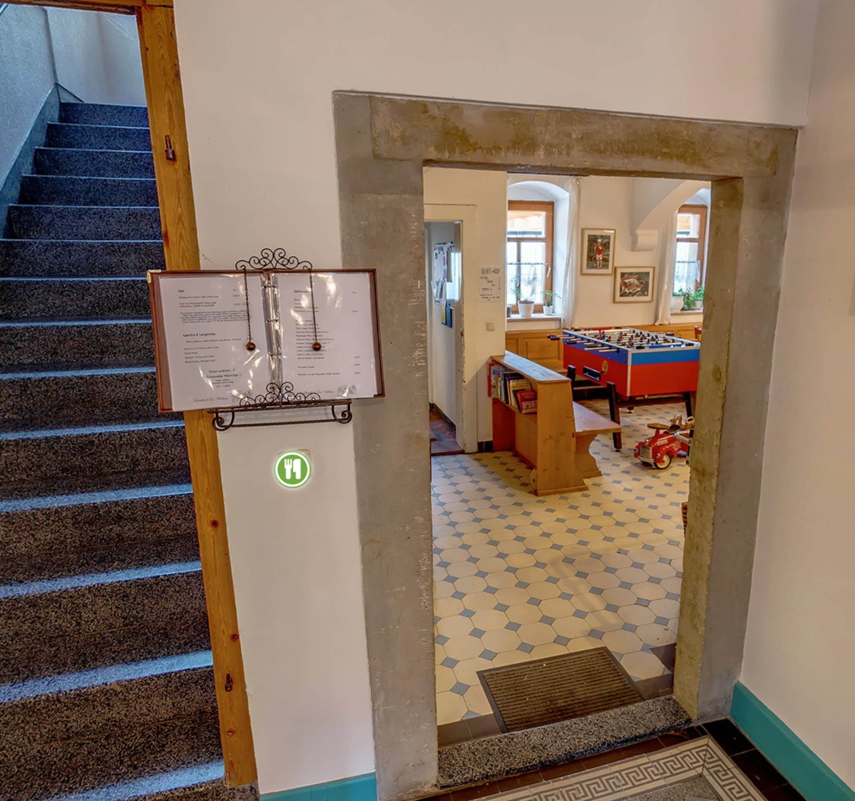 Eine Treppe führt zu einem Raum mit einem Kicker und einem Bücherregal.