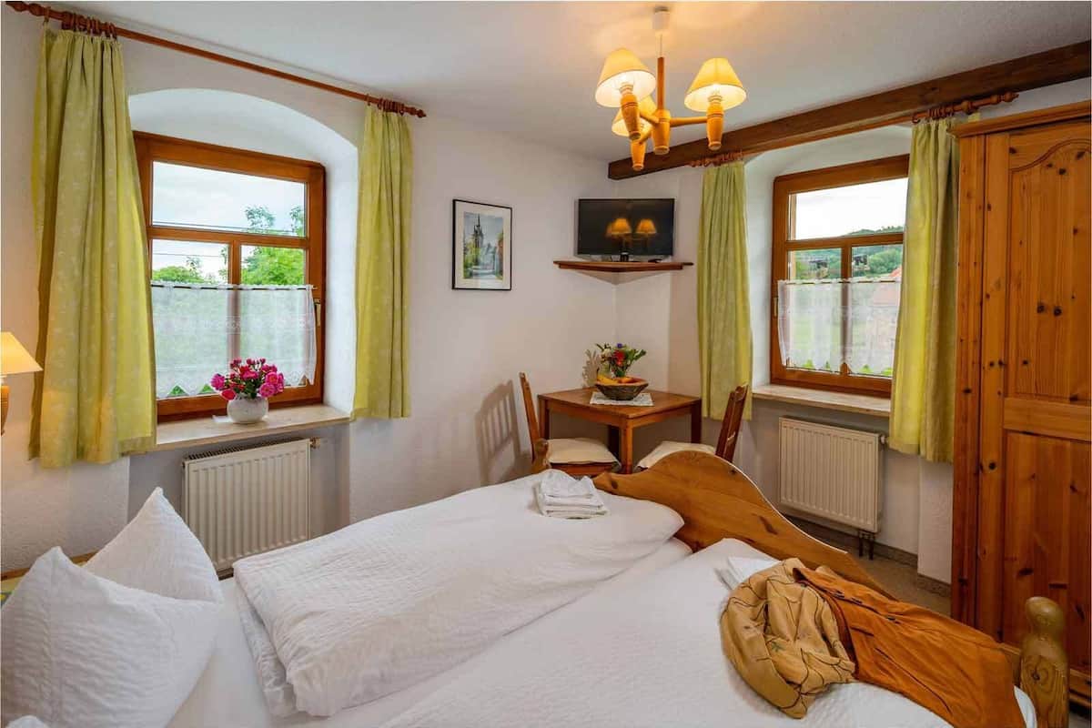A bedroom with two beds, a wooden wardrobe, a table with a vase of flowers, and a painting on the wall.