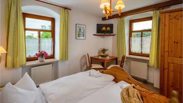 Ein Schlafzimmer mit zwei Betten, einem Holzschrank, einem Tisch mit Blumenvase und einem Bild an der Wand.
