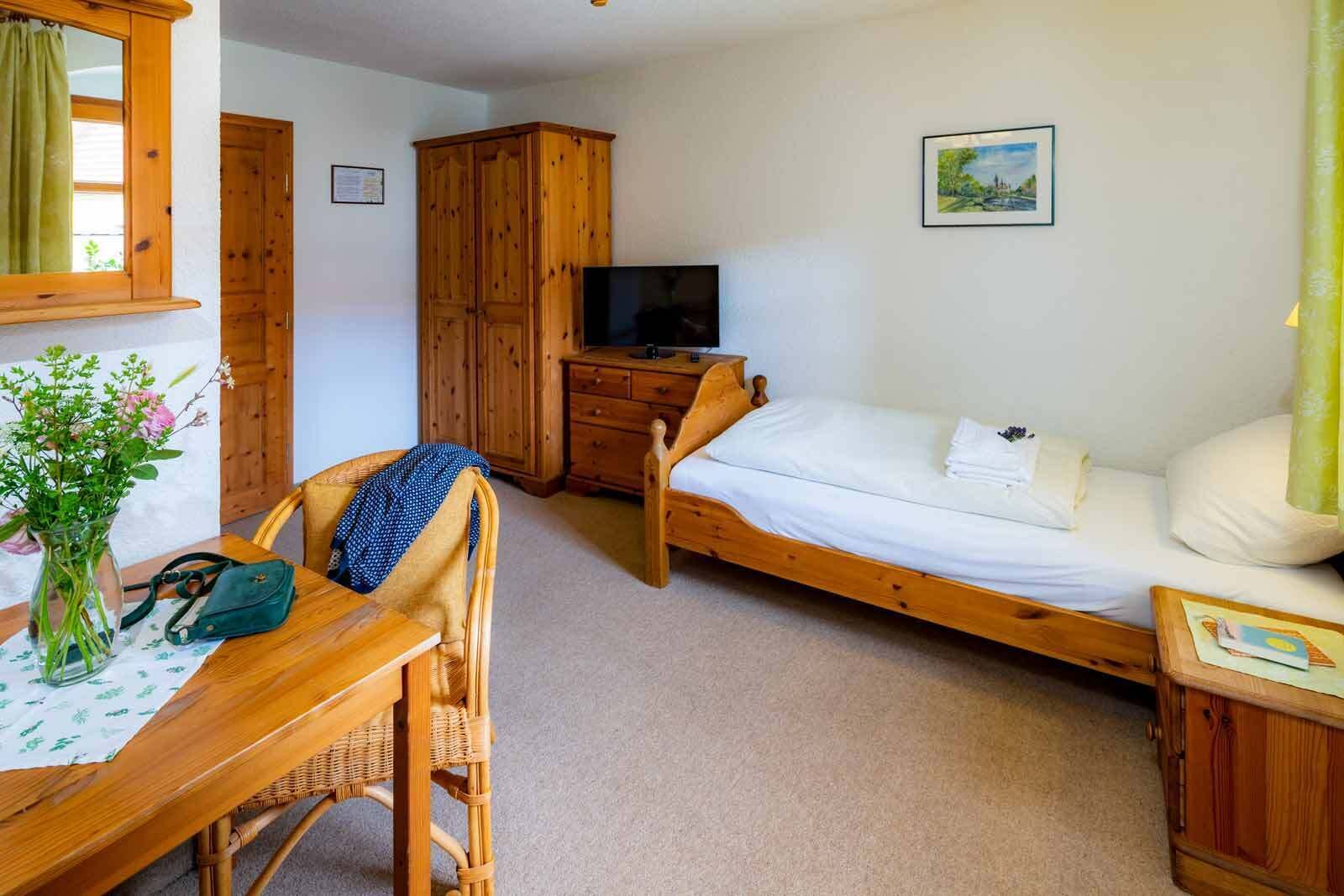 Een slaapkamer met een houten bed, een houten garderobe, een televisie en een bureau met stoel.