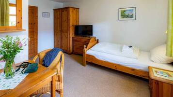 Een slaapkamer met een houten bed, een houten garderobe, een televisie en een bureau met stoel.