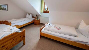 A room with three wooden beds, a small wooden nightstand, a radiator, and a window with a view of the countryside.