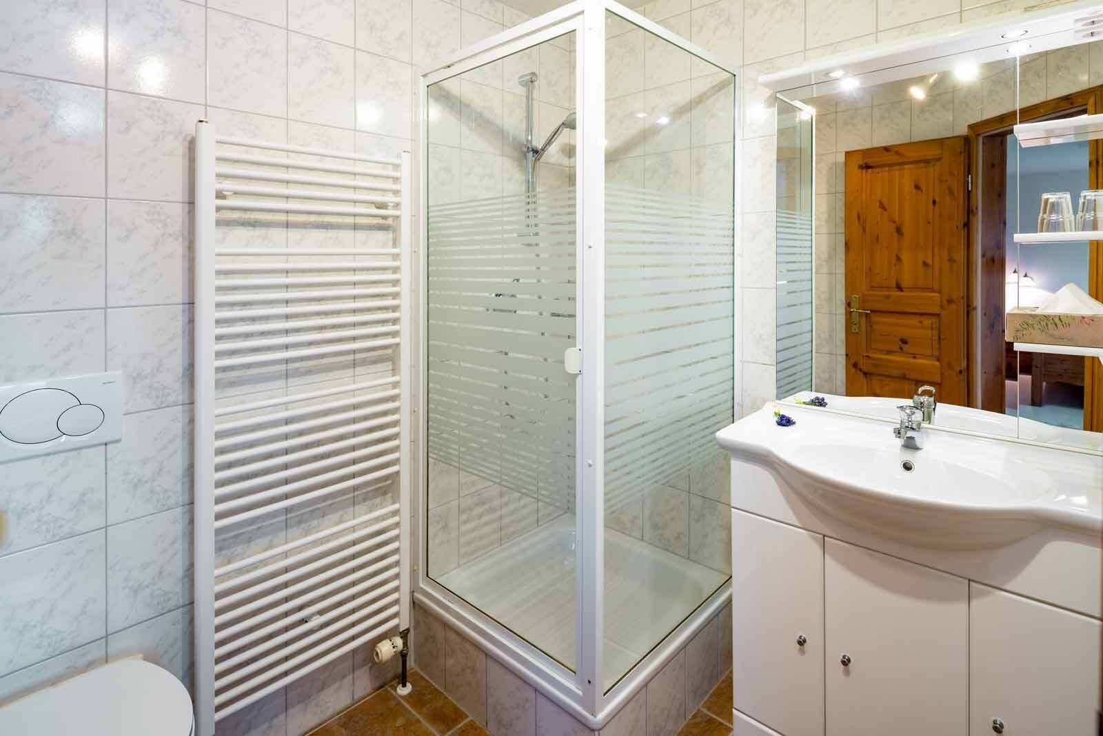 Et badeværelse med en glasafskærmet brusekabine, en hvid vask og en trædør.