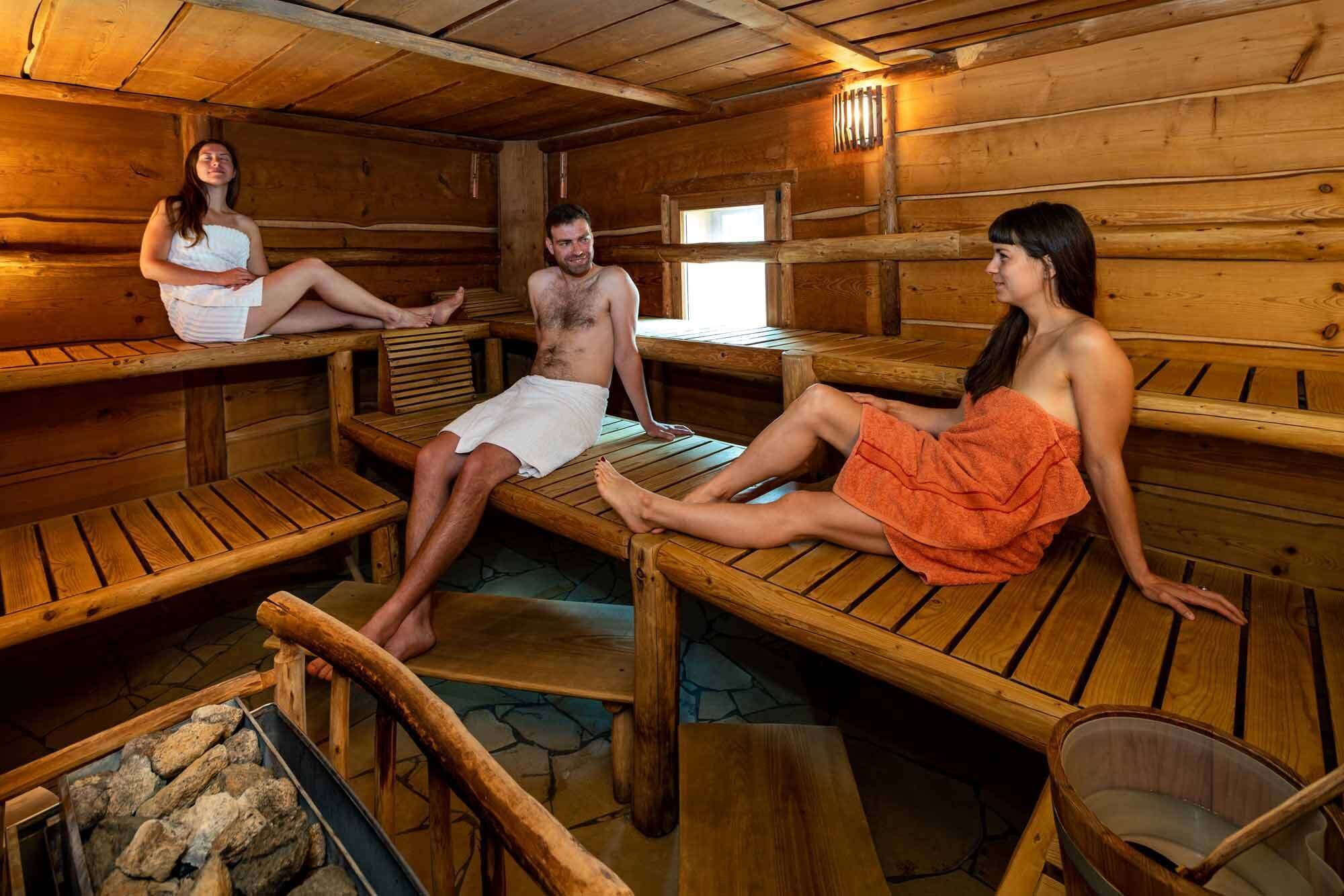 A sauna with wooden benches, a stone floor, and a stone firebox.
