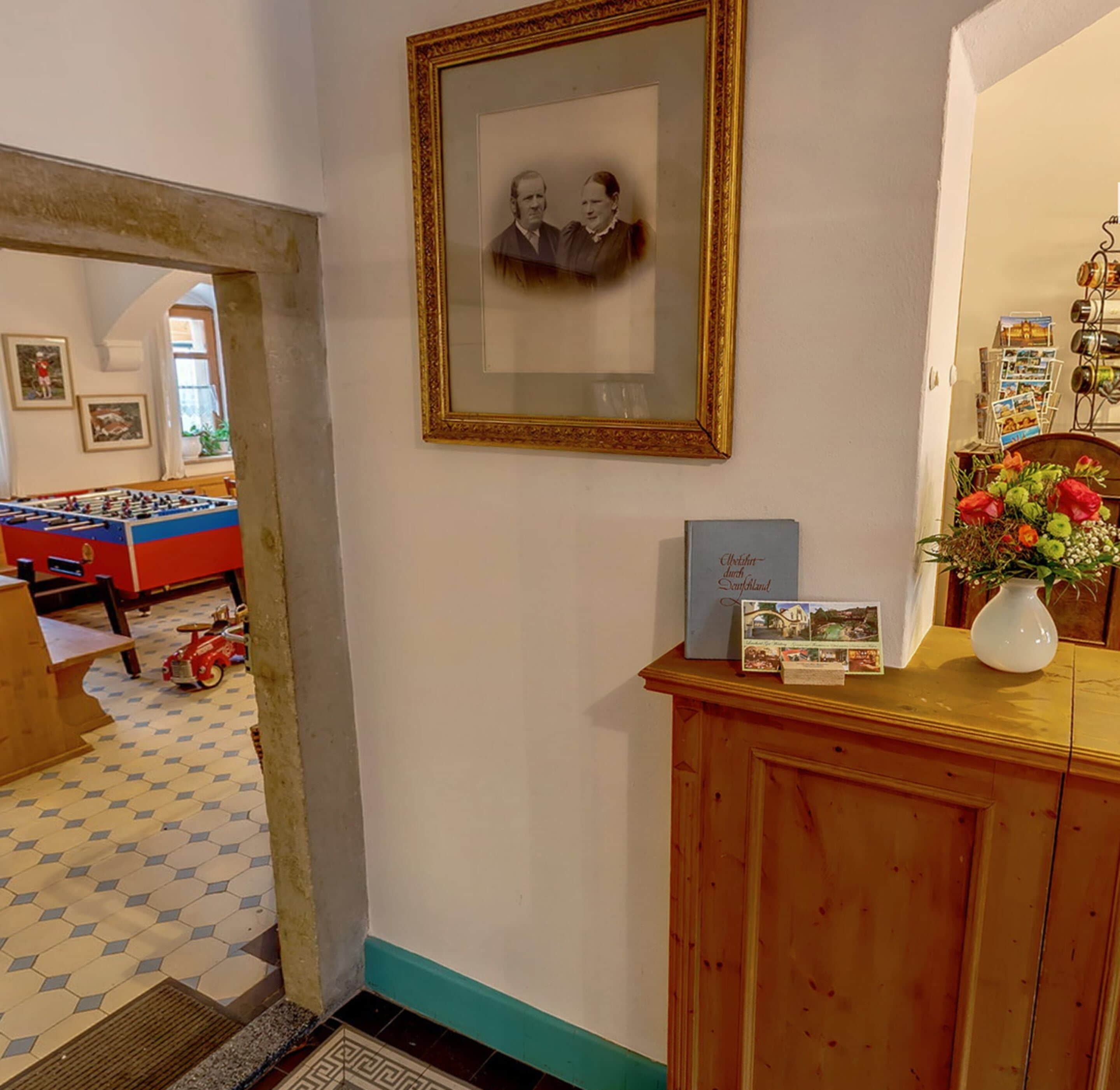 Ein Zimmer mit einem Kicker, einem gerahmten Foto an der Wand, einer kleinen Kommode mit einer Vase und einer Tür zu einem weiteren Raum.