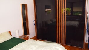 A bedroom with a bed, a bedside table, a mirror, and a sliding door leading to a balcony with a view of greenery. - Ferienwohnung AltesSalzwerk (Bad Harzburg)