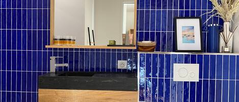 A bathroom with blue-tiled walls, a wooden vanity, a sink, and a mirror.