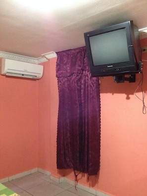 Une pièce avec un rideau violet, un téléviseur fixé au mur et un appareil de climatisation.