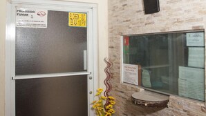 Zona de recepción con mostrador de check-in, una puerta con reja de seguridad y una lámpara fijada a la pared.