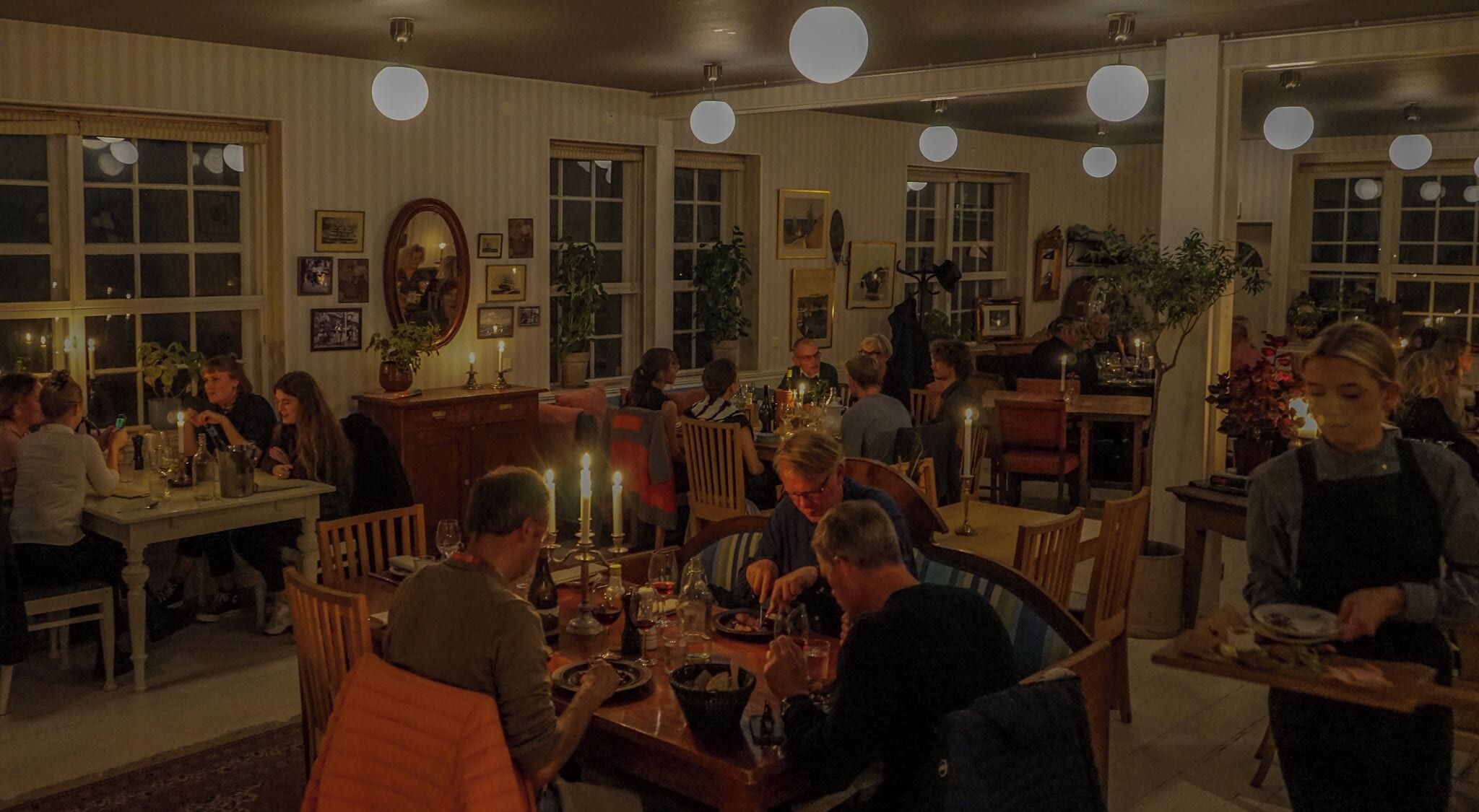 A cozy restaurant with wooden tables and chairs, candle-lit tables, and framed pictures on the walls.